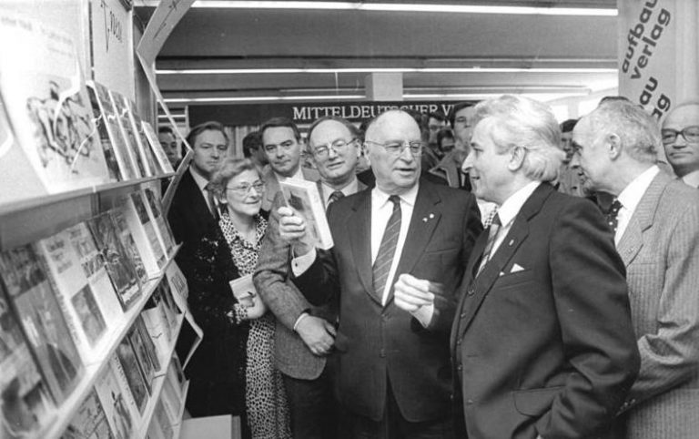 Kurt Hager (M.), Mitglied des Politbüros und Sekretär des ZK der SED besuchte bei einem Rundgang der Internationalen Leipziger Buchmesse 87 im Messehaus am Markt den Stand des Aufbau Verlages. Verlagdirektor Elmar Faber (vorn r.), gab den gästen, unter ihnen Klaus Höpke (r.), Stellvertreter des Ministers für Kultur der DDR, und Hermann Kant (M.), Präsident des Schriftstellerverbandes der DDR , Erläuterungen. | ADN-ZB Grubitzsch 15.3.87 Leipzig: Frühjahrsmesse-Buchmesse 87 via wikimedia commons